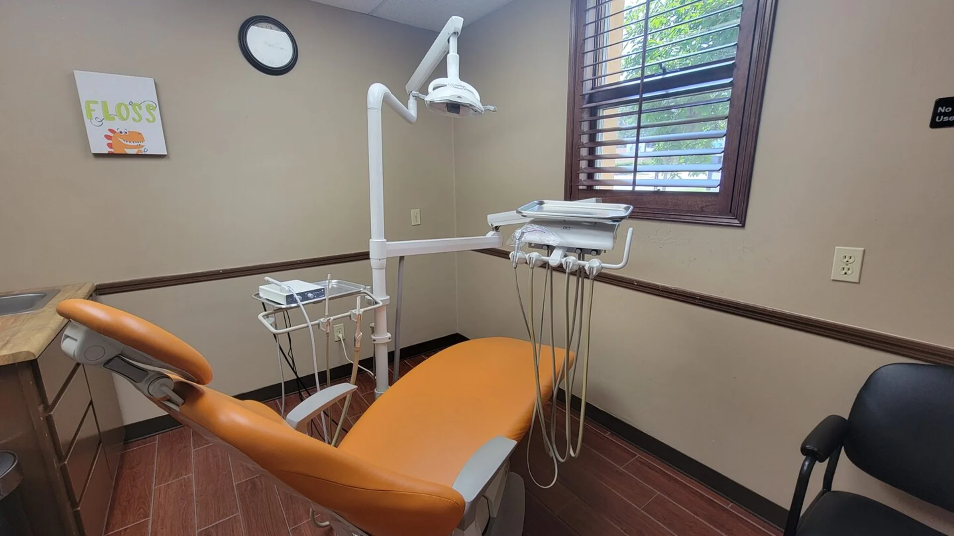 Modern dental treatment room with bright orange chair, dental equipment, and a colorful flossing poster on the wall