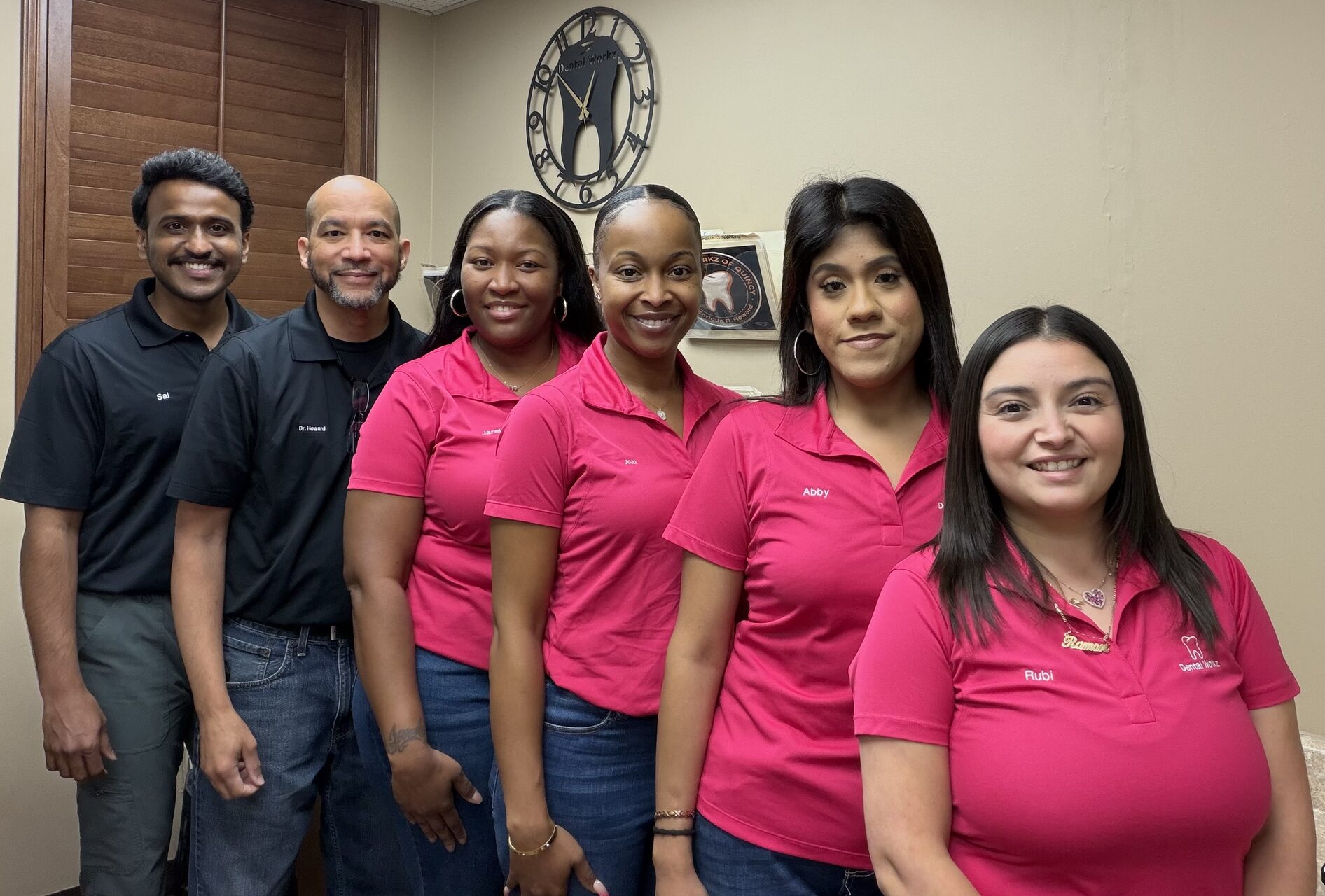 Full Dental Workz team photo featuring Sai, Dr. Howard, Jare, JoJo, Abby, and Rubi standing in front of the office tooth clock