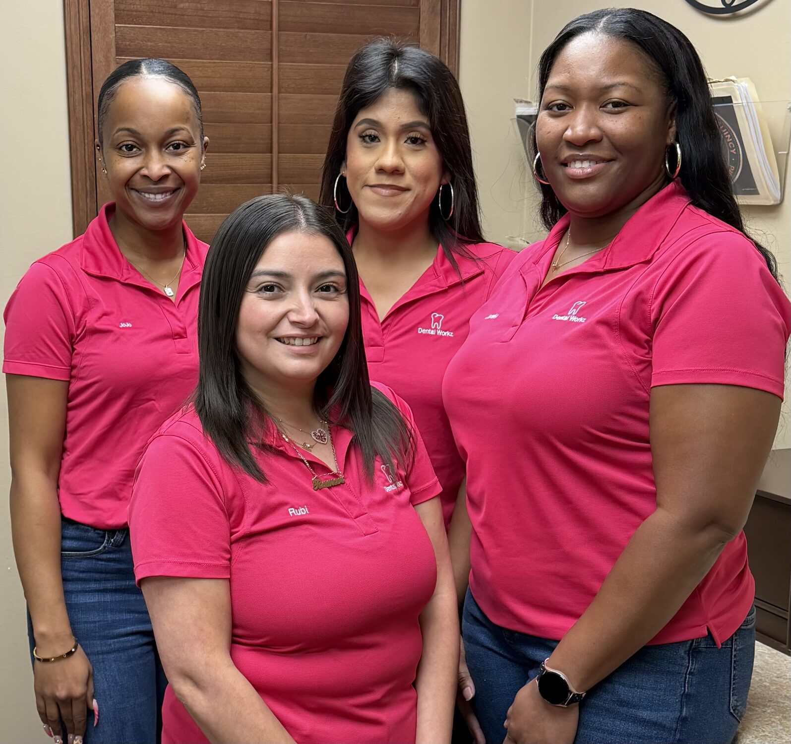 Dental Workz front desk staff members JoJo, Rubi, and Juli wearing matching pink polo shirts with embroidered names